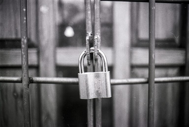 Black and white photo of a gate with a weather beaten padlock securing it